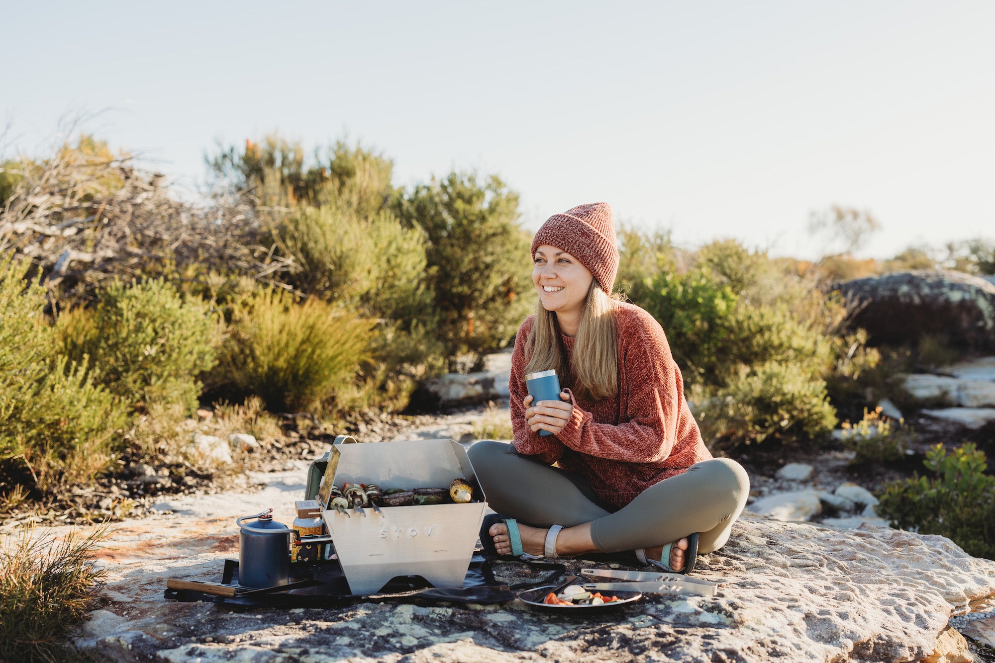 Woman bbqing on the compact STOV BBQ while holding a yeti cup